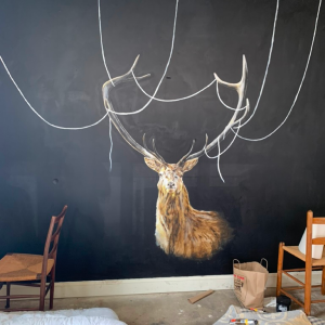 Stag mural on black wall with wooden chairs.